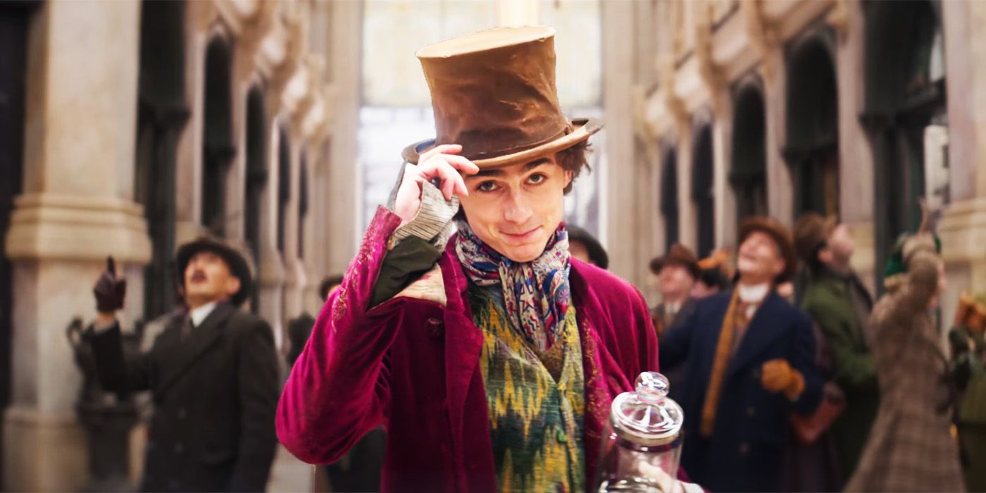 Timothee Chalamet as a young Willy Wonka tipping his hat in a crowded station in Wonka