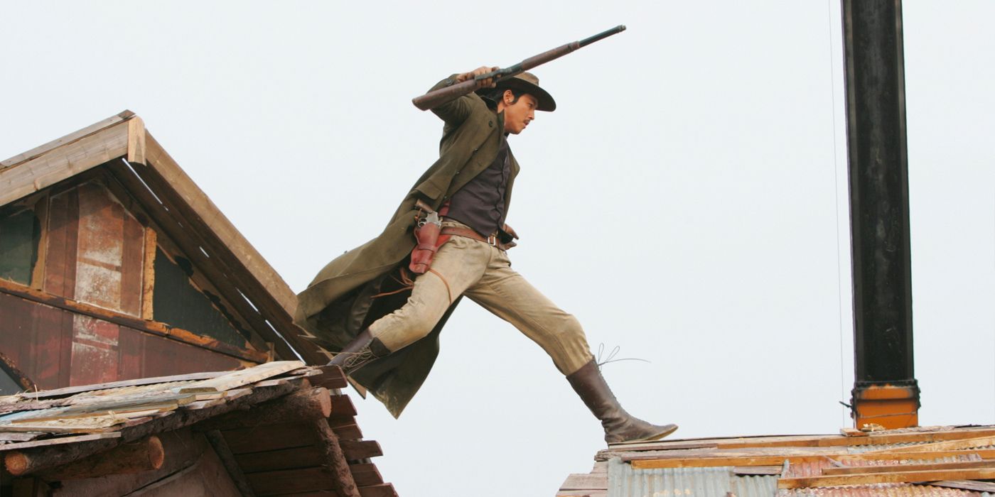 Jung Woo-sung walking across a rooftop and holding a rifle in The Good, the Bad, the Weird