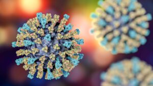 Medical illustration of a single measles virus particle with two more in the background that are blurred. The background is multi-colored. The virus particles are spherical with a purple-colored core with blue and yellow