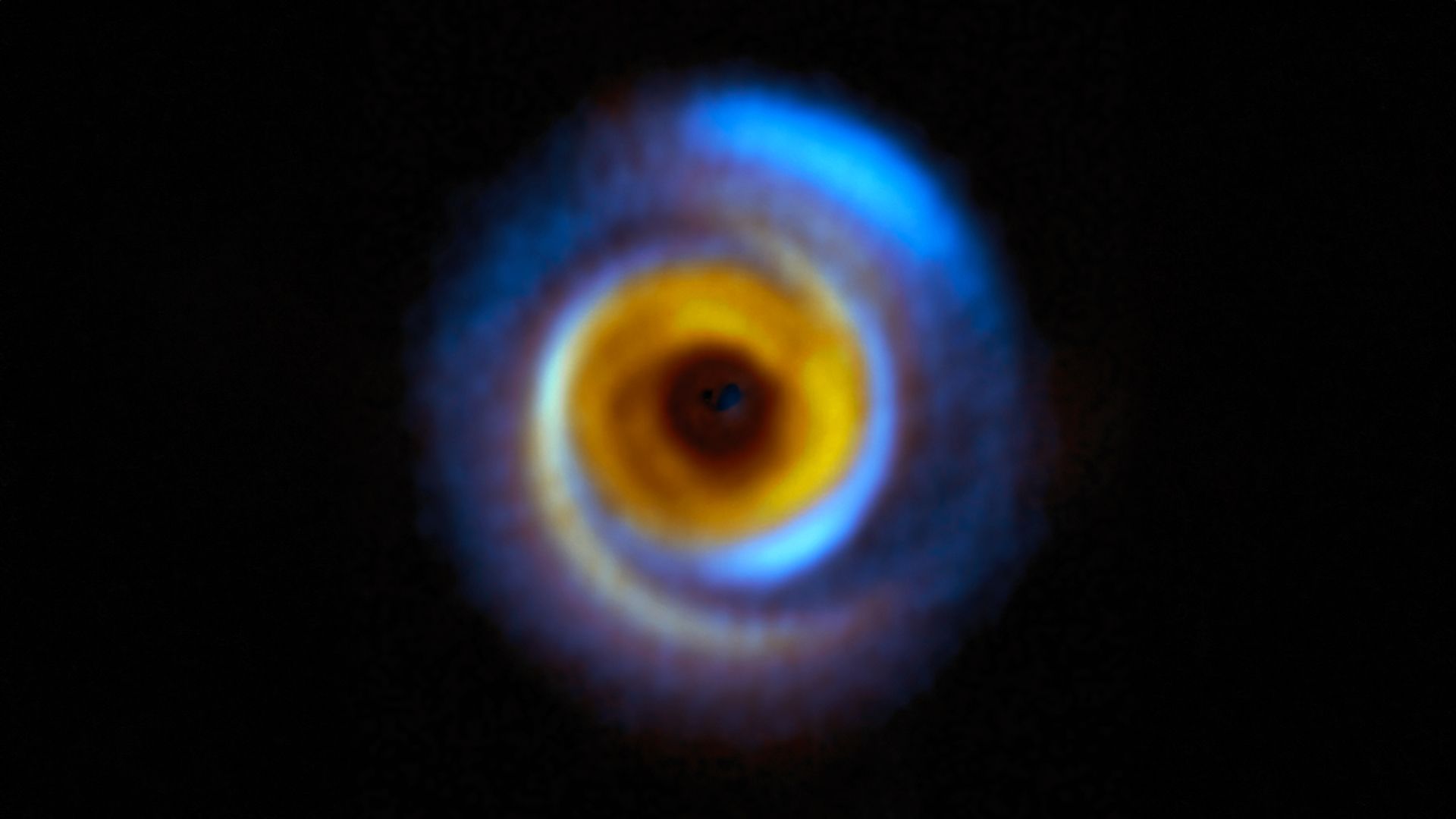 A circular blue disc with a smaller yellow disc inside. strands of both yellow and blue (different temperature material) are seen suggest the presence of forming planets.